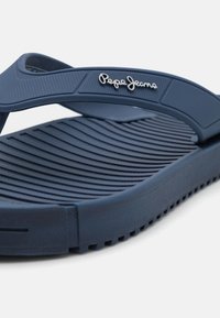 Sininen kumisaapas, jossa on teksturoitu pohja ja hihna, jossa on "Pepe Jeans" -logo valkoisilla kirjaimilla.