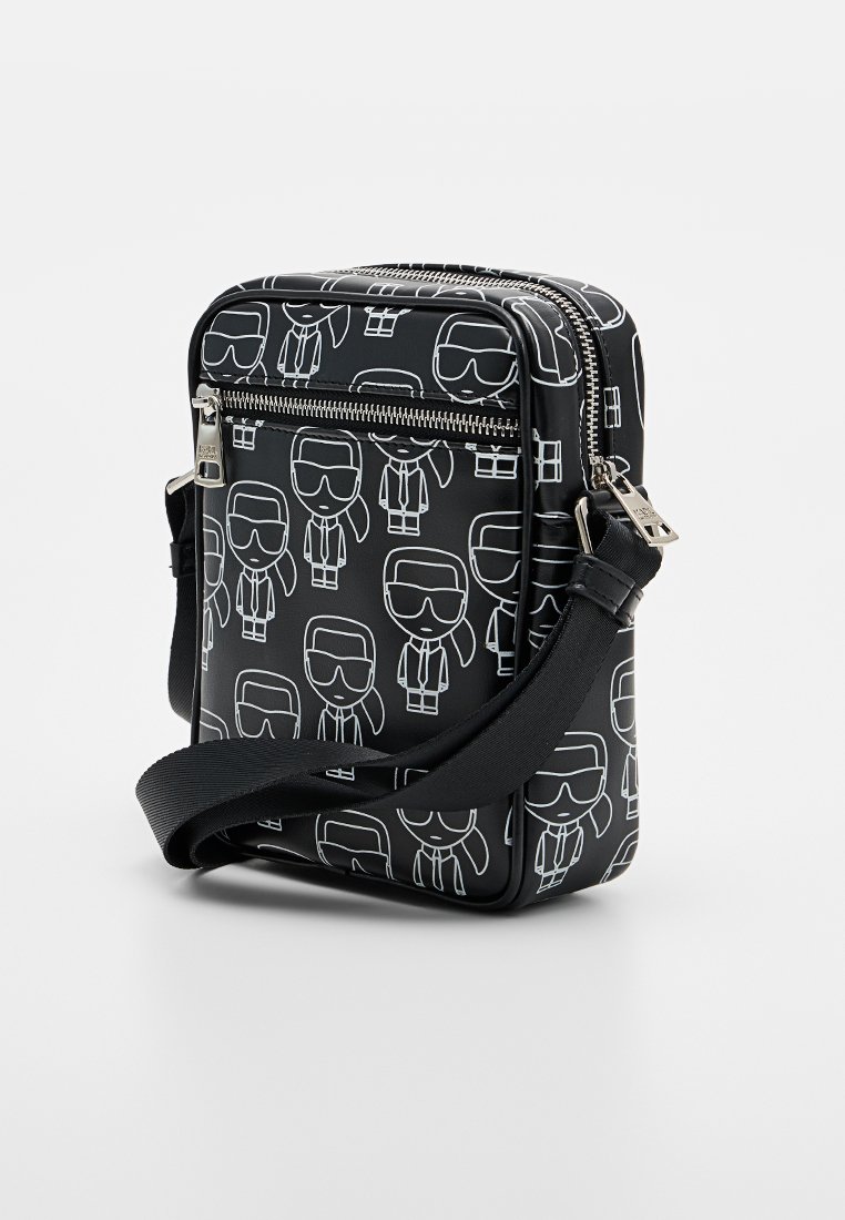 Bolso bandolera negro con estampados de personajes de dibujos animados en blanco, cierre de cremallera y correa ajustable. Hecho de material sintético liso.