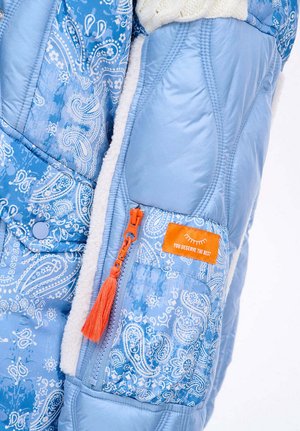 Blaue gesteppte Jacke mit Paisley-Muster, weichem Fleece-Futter, einem orangefarbenen Reißverschlussschieber mit Quaste und einem rechteckigen orangefarbenen Etikett.
