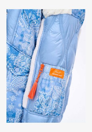 Niebieska pikowana kurtka z wzorem paisley, miękką podszewką z polaru, pomarańczowym suwakiem z chwostem oraz prostokątną pomarańczową metką.