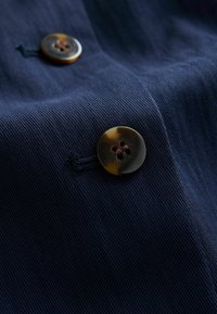 Marineblå stof med lodrette ribber og to brune, runde knapper, hver med fire huller og en glossy finish.