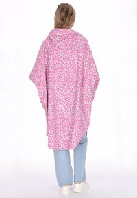 Rózsaszín leopárdmintás poncsó kapucnival, laza, lebegő kialakítással. Világoskék farmernadrággal és fehér tornacipővel párosítva.
