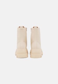 Bottines beiges en cuir lisse, dotées d'une semelle épaisse et de fermetures éclair sur le côté pour un enfilage facile. Design minimaliste aux lignes épurées.