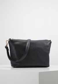 Svart läderhandväska med en strukturerad yta, försedd med en enda axelrem och dragkedjestängning. Detaljer i guldton.