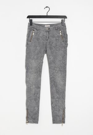 Jeans ajustados de estampado floral gris con bolsillos con cremallera y cremalleras en los tobillos, hechos de una tela texturizada. Colgados de un gancho.