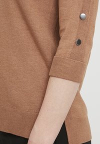 Brązowy sweter z dzianiny z rękawami o długości trzech ćwierć, z prążkowanymi mankietami, bocznymi rozporkami oraz metalowymi guzikami na rękawach.