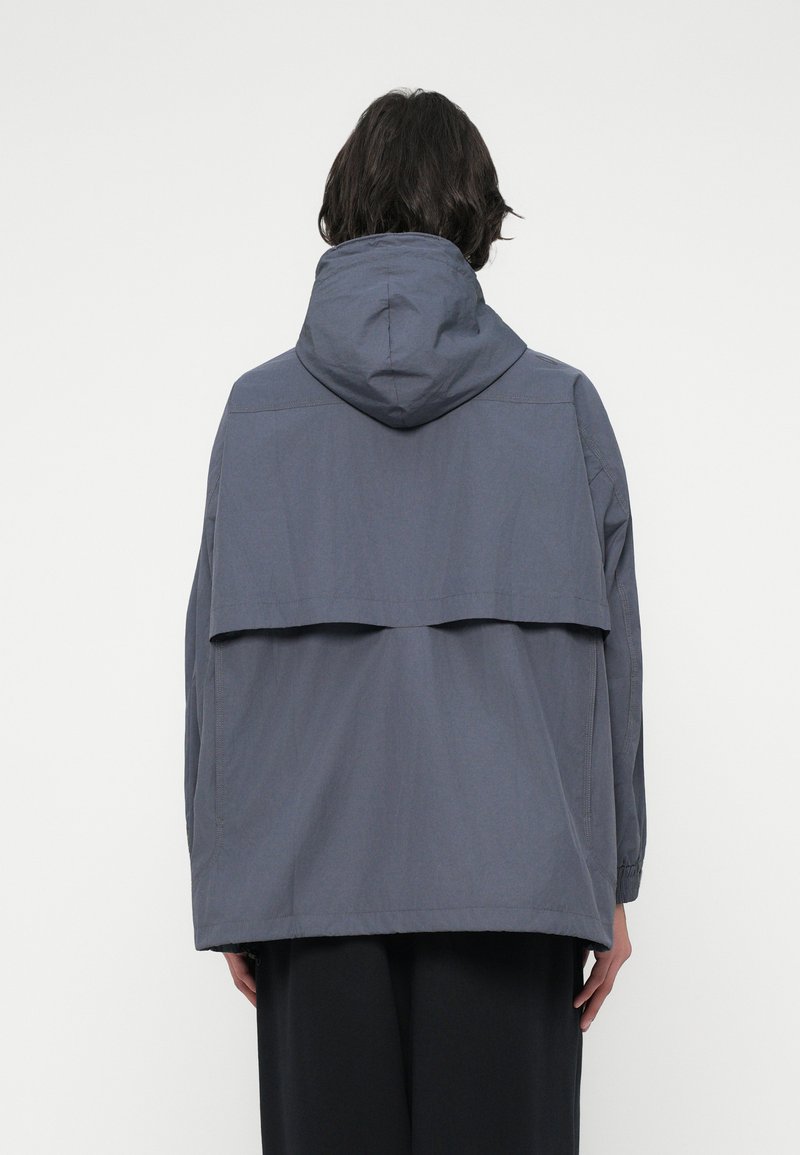 Grijze hoodie met een losse pasvorm, voorzien van een gelaagde achterkant en elastische mouwen, gemaakt van lichte stof.