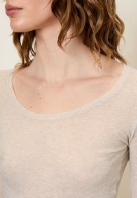 Svetlo béžový vrchný diel s dlhým rukávom a širokým výstrihom v tvare lode, s jemnou, textúrovanou tkaninou a priliehavým strihom.