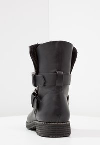 Botín negro de imitación piel con puntera redonda, dos correas laterales ajustables y forro de pelo sintético en la parte superior. Suela de goma texturizada.