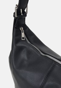 Svart läder axelväska med strukturerad yta, utrustad med en silverdragkedja och justerbar rem för anpassad passform.