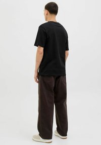 Camiseta de algodón negra de manga corta, combinada con pantalones sueltos de color marrón oscuro y zapatillas blancas. Diseño simple y minimalista.
