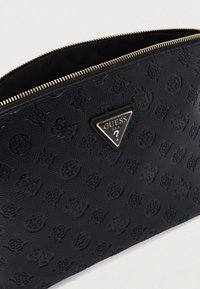 Μαύρο θήκη από συνθετικό δέρμα με υφή, με ανάγλυφο σχέδιο και χρυσή τριγωνική πλακέτα λογότυπου με την επιγραφή "GUESS U.S.A." και ένα ερωτηματικό.