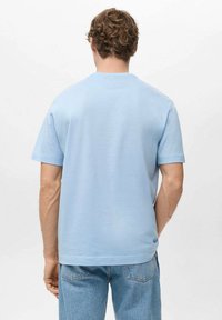 Světle modré bavlněné triko s krátkými rukávy, kulatým výstřihem a hladkou texturou, zobrazené zezadu s volným střihem.