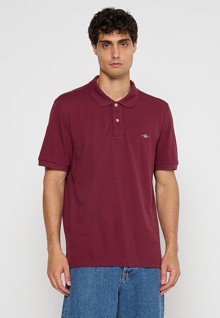 Polo en bourgogne en coton, avec un col, une patte de boutonnage à trois boutons et un petit logo sur la poitrine gauche. Manches courtes, coupe classique.