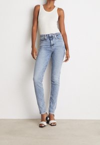 Ljust blå högmidjade jeans i denim, med smal passform och femfickdesign, kombinerade med en vit linne och tvåfärgade klackar.