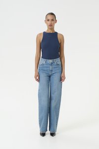 Ναυτικό ριμπαρισμένο τοπ με ψηλή λαιμόκοψη; ανοιχτό μπλε παντελόνι σε φαρδιά γραμμή με πέντε τσέπες και θηλιές ζώνης; μαύρες γυαλιστερές γάμπες.