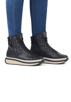 Baskets montantes en cuir noir avec une finition texturée, dotées d'une fermeture éclair latérale, de lacets et d'une semelle épaisse couleur crème. Portées avec un jean bleu.