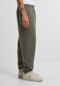 Olive green sweatpants made of soft material with an elastic waistband, side pockets, and cuffed hems, paired with beige sneakers.