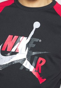 Camiseta negra de manga corta roja con un gran diseño gráfico que dice "NIKE AIR" en rojo y blanco, acompañado de un logo de figura saltando.