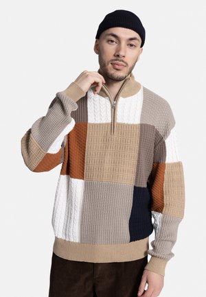 Knit zip-up sweater featuring a patchwork design in beige, brown, navy, and white. Textured fabric with ribbed cuffs and hem.