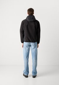Schwarze Jacke mit einer gepolsterten Kapuze, elastischen Bündchen und einer glatten Stoffoberfläche, kombiniert mit hellblauen, locker sitzenden Jeans und dunklen Schuhen.