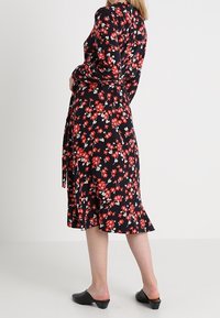 Musta kukkamekko punaisilla ja valkoisilla kuvioilla, pitkät hihat, sidottu vyötärö ja levenevä helma. Yhdistetty mustiin liukuhihna-kengiin.