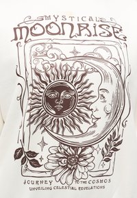 Λευκό ύφασμα με καφέ γραφικό ενός ήλιου και φεγγαριού, περιτριγυρισμένο από ανθικά στοιχεία και διακοσμητικές λεπτομέρειες, με κείμενο που γράφει «Μυστικοπαθής Ανατολή Σελήνης».