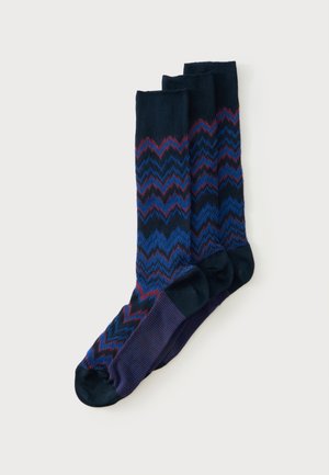 Trois paires de chaussettes bleu marine avec des motifs en zigzag dans des nuances de bleu, violet et rouge, présentées à plat avec les orteils pointant vers la gauche.