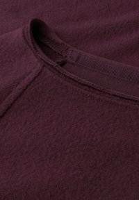 Bordeaux stof met een zachte, textuurrijke oppervlakte en een ronde hals. Zichtbare stikseldetails langs de kraag. Casual ontwerp.