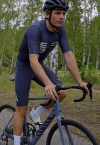 Cyklista na šedých bicykli Canyon, oblečený v námorníckej dresu s bielymi akcentmi. Obklopený zeleňou, s hladkou cestou na dohľad.