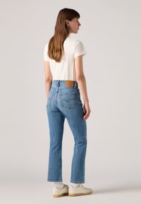 Jean bleu taille haute en denim avec un délavage clair, présentant une pièce en cuir marron à l'arrière et une coupe droite.