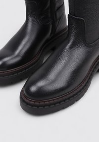 Botas de tobillo de cuero negro con un acabado texturizado, puntera redonda y suela de goma resistente con detalles de costura en contraste.