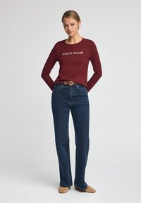 Bordeaux långärmad skjorta med texten "POLO CLUB", kombinerad med mörk denimflared jeans och ljusbruna slip-on skor.