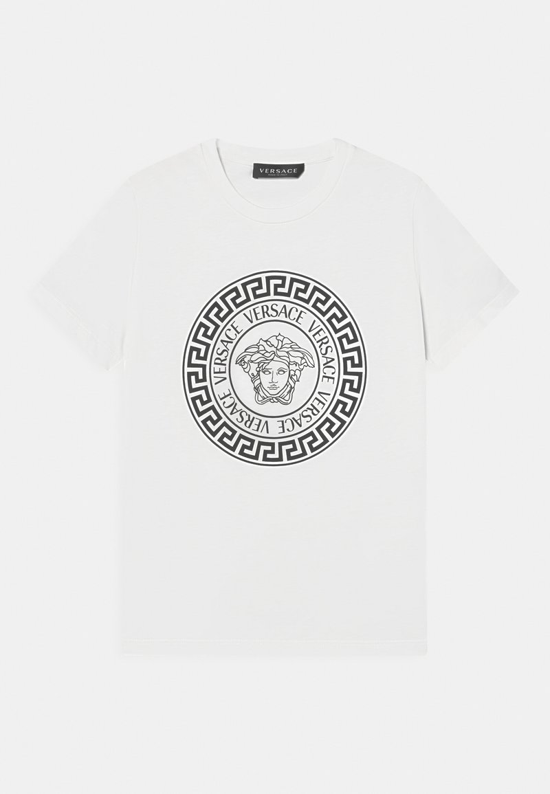 Bílý bavlněný tričko s černou grafikou Méduzy uvnitř kruhového řeckého klíčového vzoru, s nápisem "VERSACE" opakovaným kolem designu.