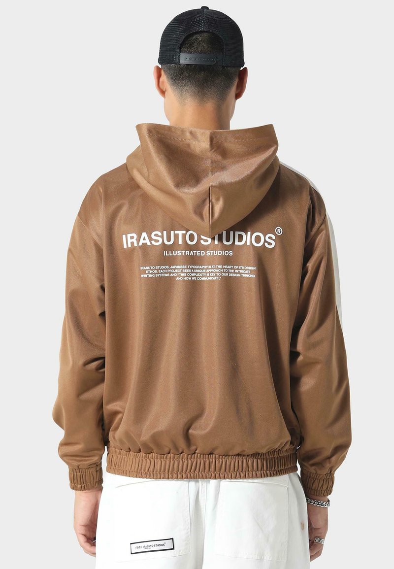 Bruine hoodie-jack met elastische zoom en manchetten, voorzien van witte branding op de achterkant. Het materiaal lijkt glad en licht van gewicht.