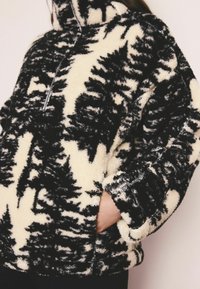 Pulover din fleece cu un model alb-negru, guler cu jumătate de fermoar și buzunare laterale. Textură moale și croială relaxată cu mâneci largi.