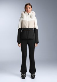 Ski jakna s kapuljačom od umjetnog krzna, s kuretom u bež boji i crnom donjom polovinom, s pojasom u struku, te pripadajućim crnim hlačama s proširenim rukavima.