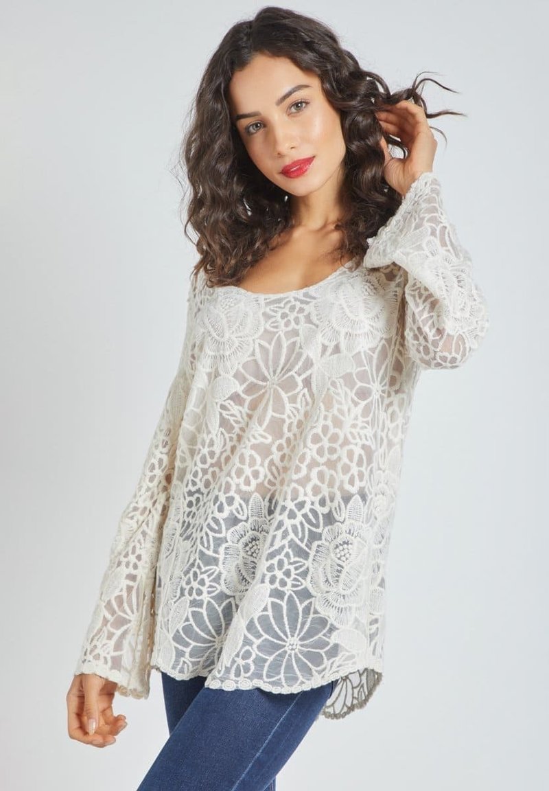 Top de encaje en color blanco roto con patrones florales, mangas largas y acampanadas, y un corte holgado. Textura transparente con dobladillo con forma de ondas.