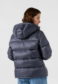 Marineblauwe gewatteerde jas met een capuchon, met een gestikt ontwerp en doorgestikte secties. Gladde, glanzende textuur met elastische manchetten.