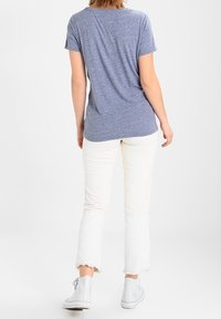Blue heathered short-sleeve t-shirt paired with white cropped pants featuring frayed hems and gray high-top sneakers.