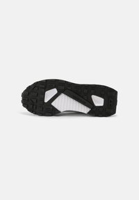 Black rubber shoe sole with prominent tread pattern, white midsole, and distinct geometric shapes for traction and support.