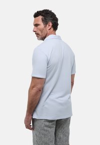 Polo-shirt bleu clair à manches courtes, en tissu doux. Présente un col classique et une coupe ajustée. Porté avec un short rayé gris clair.