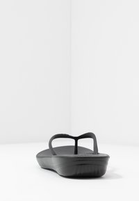 Tongs noires en caoutchouc flexible. Dotées d'une semelle intérieure texturée et de brides fines pour un ajustement sécurisé. Semelle basse et profilée.