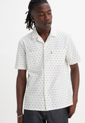 Biała koszula z krótkim rękawem, z niebieskim geometrycznym nadrukiem, z kołnierzykiem zapinanym na guziki, jedną kieszenią i logo Levi's na klatce piersiowej. Wykonana z bawełny, o luźnym kroju.