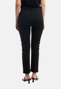 Pantaloni neri sartoriali con una vestibilità slim, caratterizzati da una texture liscia e con risvolti, abbinati a sandali neri con apertura sulle dita. Vista posteriore mostrata.