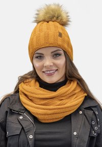Knit orange beanie with a faux fur pom-pom, paired with a matching textured scarf. Both items display a ribbed pattern and warm texture.