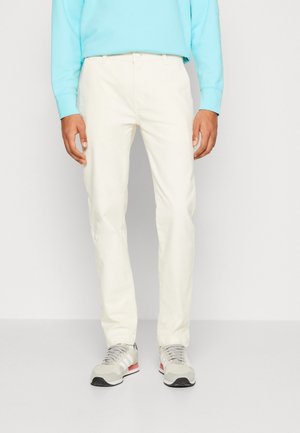 Mann trägt off-white gerade geschnittene Hose, kombiniert mit grauen und weißen Turnschuhen und einem türkisfarbenen Langarmshirt.