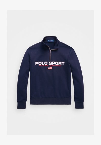 Tamnomač v mornarsko modri barvi z zadrgo, narejen iz mešanice bombaža, s poudarjenim napisom "POLO SPORT" v debelih belih in rdečih črkah ter grafiko ameriške zastave.