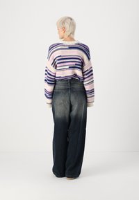 Heklet genser med lilla og rosa striper, kombinert med høyt liv, løstsittende blå jeans med en gradient fra mørk til lys.