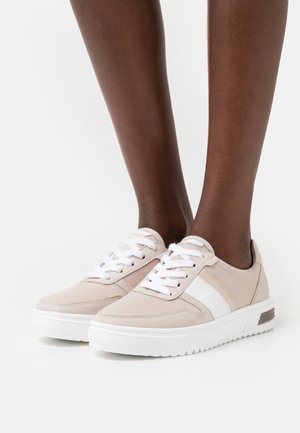 Zapatillas beige con acentos blancos, diseño con cordones, tela texturizada y suela blanca gruesa. Presentan un pequeño detalle de tacón transparente.